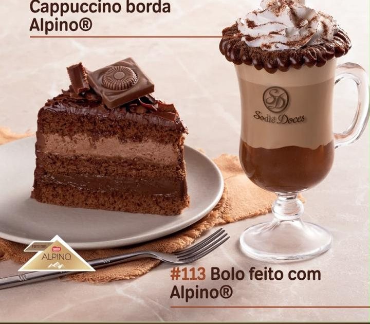 Cappuccino com borda de chocolate Alpino ao lado de fatia de bolo de chocolate.