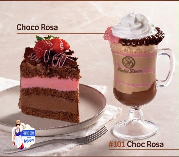 Cappuccino com borda rosa e chocolate ao lado de fatia de bolo de chocolate com recheio rosa.